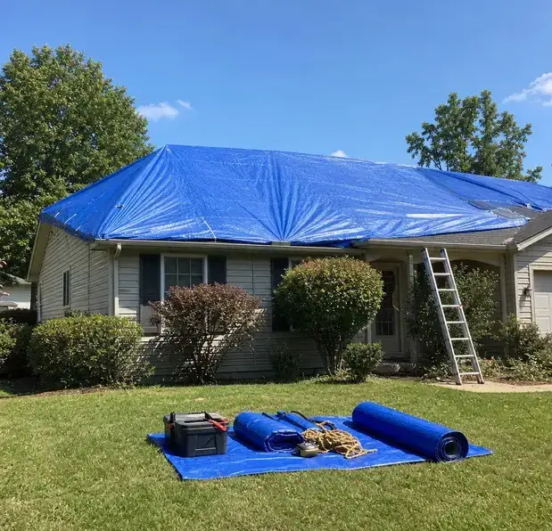 Blue roof tarp secured over a house with a ladder and spare tarps on the lawn in Bay Village, OH