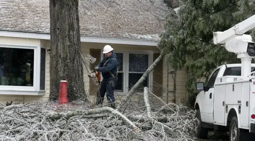 Worker clearing ice-covered fallen branches beside a home after a winter storm in Bay Village, OH